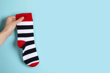 Woman holding striped sock on light blue background, closeup. Space for text