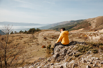 Fototapeta premium Man in a yellow jacket sitting on the rock among the mountains at sunny day in the forest in Turkey Bolu. Hiking concept