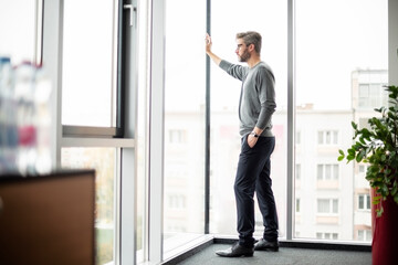 Shot of thinking businesman standing at the office and looking out of city