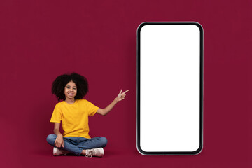 Happy black preteen girl pointing at big cell phone, mockup