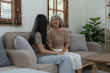 Loving adult daughter hugging older mother on couch at home, family enjoying tender moment together, young woman and mature mum or grandmother looking at each other, two generations