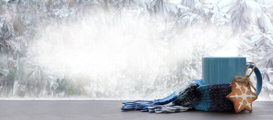 glazed cookies and blue mug wrapped in scarf against frozen window. warming drink on winter morning