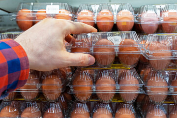 Chicken eggs on the store shelf. A customer takes a packaging of chicken eggs from a supermarket fridge. Containers of chicken eggs in a refrigerator store.