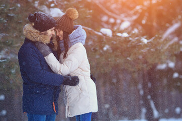 Happy young man and woman hugs in winter forest, sunlight. Romantic relationship of couple in love, copyspace