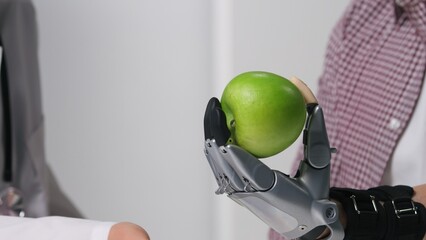 Close up of patient hold apple in bionic arm while visiting doctor in modern clinic