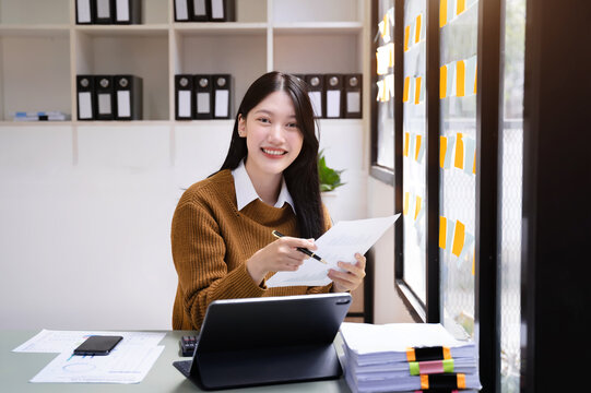 Smiling young asian woman succeeding in business using laptop and computer while doing some paperwork at office.