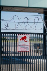 Vertical of a warning sign on the gate and barbed wire at Lech Walesa airport in Gdansk, Poland. - obrazy, fototapety, plakaty