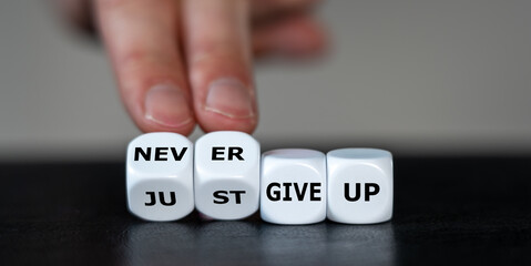 Hand turns dice and changes the expression 'just give up' to 'never give up'.