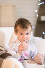 Fototapeta premium little boy, holding a ball of yarn for knitting in a box, sitting in an armchair in a cozy room