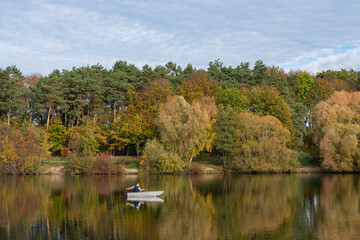Naklejka premium Autumn trees are reflected in the lake on which a motor boat floats. Beautiful water landscape.
