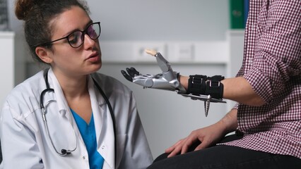 Young female therapist examine patient moving hand prosthesis in hospital