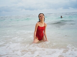 Sexy woman in a red swimsuit with an athletic body stands in the water in the ocean and poses looking out at the horizon