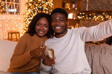 Happy young african american couple cheers with champagne glasses, make selfie, video call
