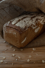 A loaf of bread on a bamboo board, sprinkled with oat flakes, in a burlap bag with garlands
