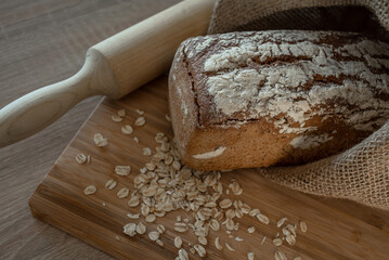 A loaf of bread on a bamboo board, sprinkled with oat flakes, in a burlap bag with garlands