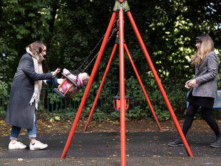 Female couple swinging baby in park