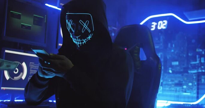 A hacker wearing a mask to cover his face is using computer to hack data to get ransom from victims.