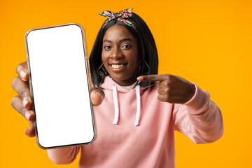 Portrait of a excited young african woman showing blank screen mobile phone over yellow background