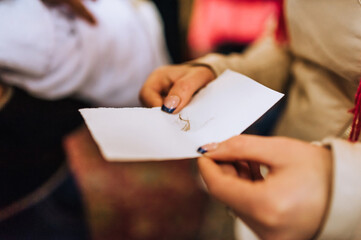 Mom, woman, godmother holds a paper with the hair of a newborn child after the haircut ceremony in the church. Close-up photography, religion.