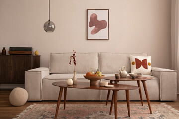 Domestic and cozy interior of living room with mock up poster frame, modern beige sofa, oval wooden coffee table, round pillows, braided plaid, vintage rug, wooden floor, lamp and personal accessories