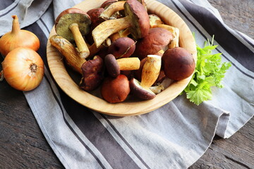 Forest boletus mushrooms on rustic wooden background in wooden bowl and herbs