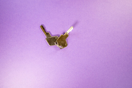 close up of a pair of silver padlock keys - one bent out of shape isolated on a purple background