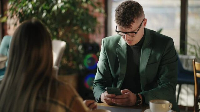 man and woman are having lunch in cafe, attractive man is sending message by mobile phone, chatting online