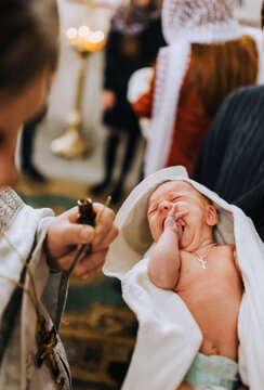 A male Christian priest in a church conducts a sacred rite, a ritual for a newborn crying child, in the arms of a godfather. Photography, religion.