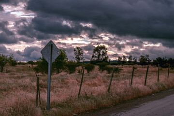 Camino de tierra con un letrero sin señal con cielo de nubes después de la lluvia en un ambiente oscuro en el campo rural