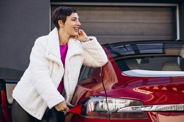 Woman charging electro car with charging pistol by the house