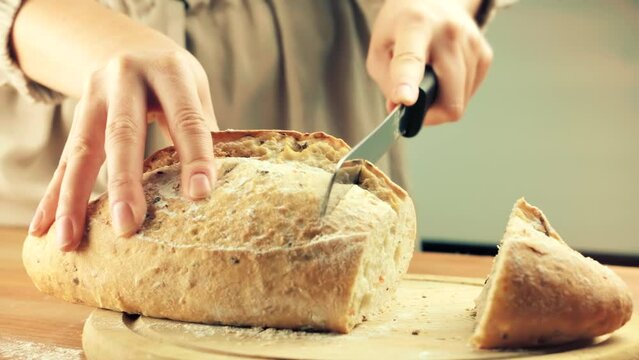 A loaf of fresh bread is being sliced on a table using a sharp knife