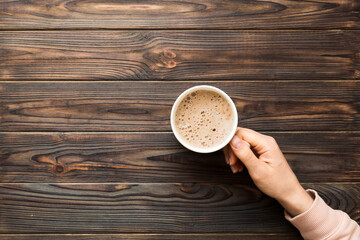 Minimalistic style woman hand holding a cup of coffee on Colored background. Flat lay, top view cappuccino cup. Empty place for text, copy space. Coffee addiction. Top view, flat lay