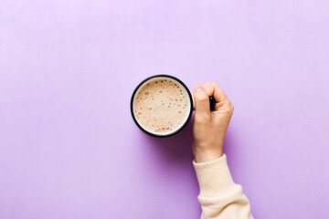 Minimalistic style woman hand holding a cup of coffee on Colored background. Flat lay, top view...