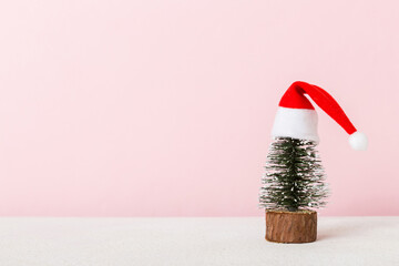 One small Christmas tree with santa hat on colored background. new year decoration with copy space