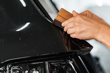 Close up of car wrapping specialist putting protective film on a car in detailing service - obrazy, fototapety, plakaty
