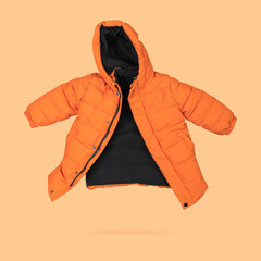 Orange flying children's winter autumn jacket with hood isolated on light orange background. Waterproof jacket for child, warm down jacket. Cutout clothing mockup. Fashion, style, outerwear