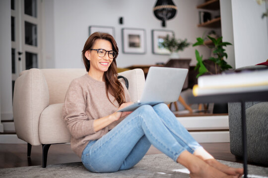 Smiling caucasian woman using laptop at home while sitting on the floor