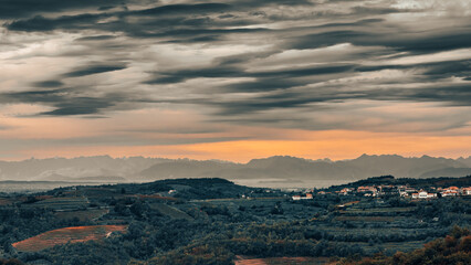 Scenic landscape at Šmartno, Brda Goriska, Slovenia. Vineyards with mountain chain in background under a dramatic sky. - obrazy, fototapety, plakaty