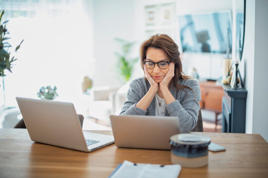 Portrait of an attractive business woman using a laptop while working in her home office. Confident female wearing eyeglasses and grey cardigan.
