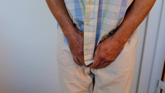 man in beige trousers, male hands on groin, mature man wants to go to toilet, senior 60 years old feels discomfort, concept of men's health, age-related urinary incontinence