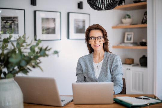 Shot of an attractive business woman using a laptop while working in her home office. Confident female wearing eyeglasses and grey cardigan.
