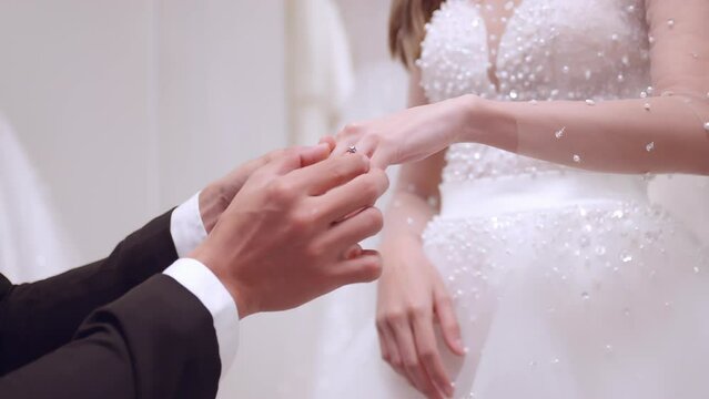 Groom putting wedding ring on finger of bride.