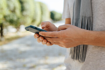 Close-up of man using smartphone in park. Side view of male caucasian hands typing messages on mobile phone screen outdoors