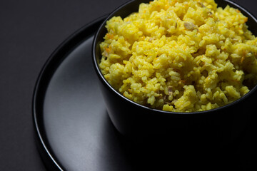 Yellow pilaf in a black plate on a black background. Traditional oriental dish