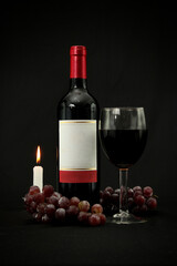 Bottle of wine accompanied by a glass, bunches of grapes and candle