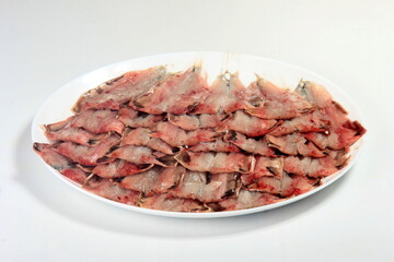 many opened and cleaned small fish on a plate on a white background