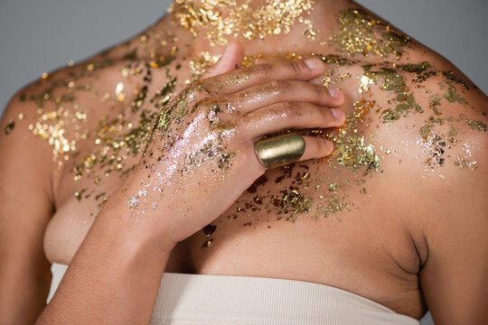 Cropped view of young african american woman touching golden foil on body isolated on grey.
