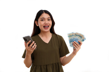 Happy beautiful young asian lady standing while holding Indonesian banknotes and cell phone. Isolated on white