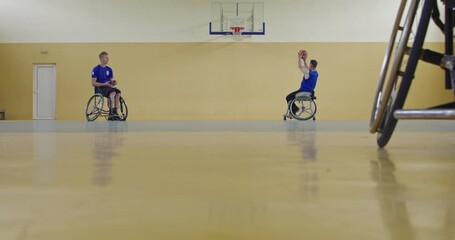 Close-up of a sporty person with disability sitting in a wheelchair playing a basketball team game in the school gym court. Selective focus. 