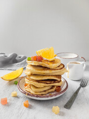 Fritters are stacked on a plate, poured with honey and decorated with an orange slice and dried fruits.